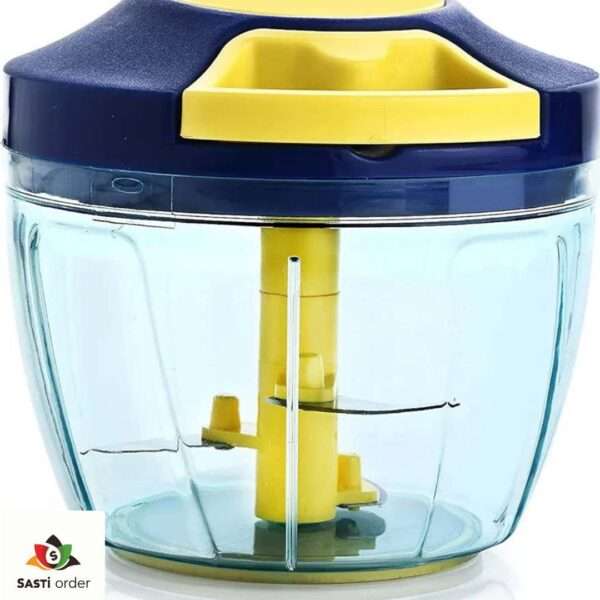 A Manual Vegetable Fruit Onion Chopper with a clear bowl, stainless steel blades, and a pull-cord mechanism, placed on a kitchen counter with chopped onions and vegetables nearby.