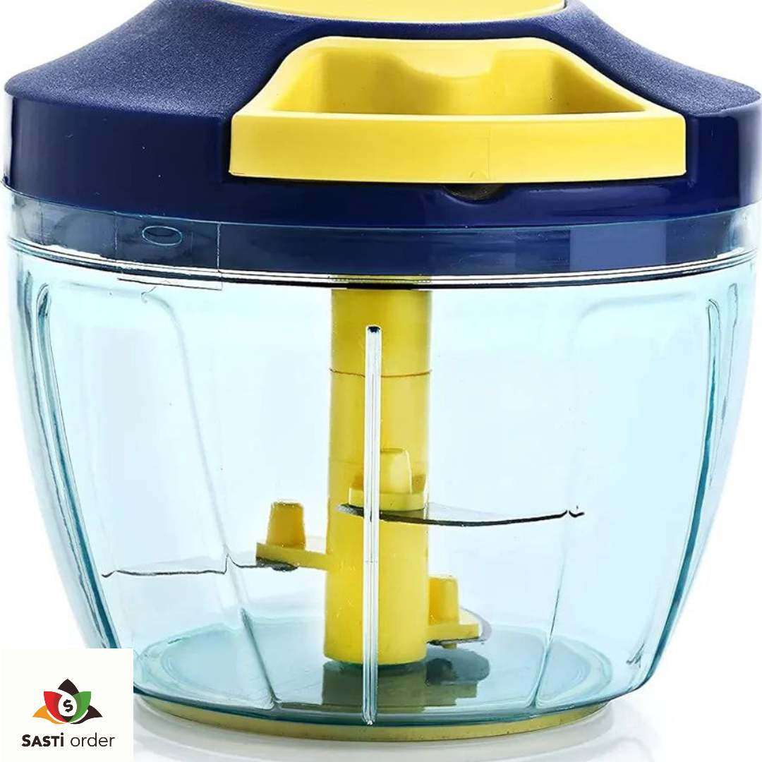 A Manual Vegetable Fruit Onion Chopper with a clear bowl, stainless steel blades, and a pull-cord mechanism, placed on a kitchen counter with chopped onions and vegetables nearby.